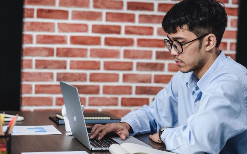 A focused man in glasses working on his laptop, deep in concentration.